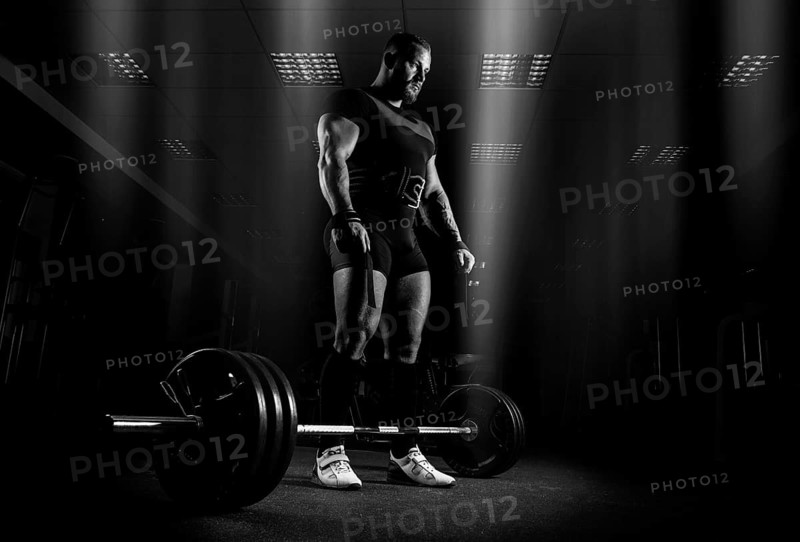 The weightlifter is preparing to perform an exercise called deadlift. He stands directly above the barbell and looks at it