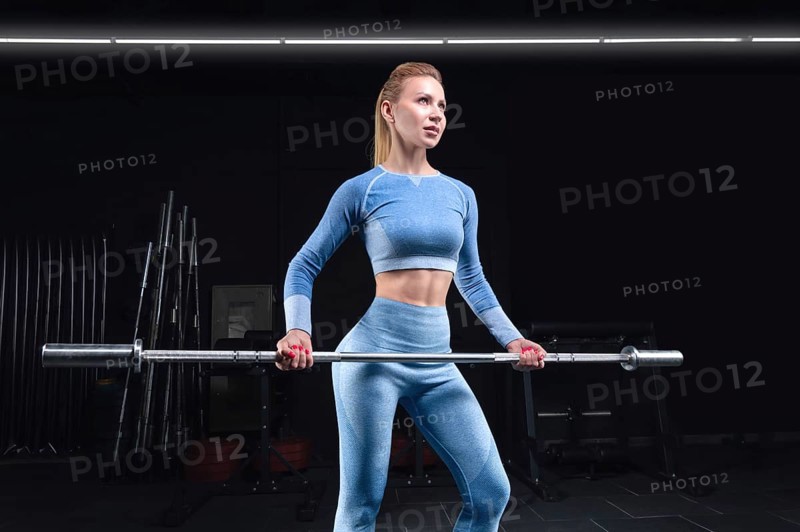 Athletic physique woman posing with a barbell in her hands. The concept of sports