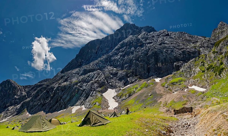 Tents of mountain hunters in the foreground with imposing mountain cliffs and blue sky with foehn clouds in the background
