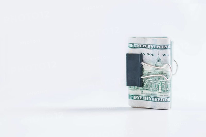 Pack of hundred-dollar bills lies on a white table fastened with a paperclip. The concept of savings during the crisis.