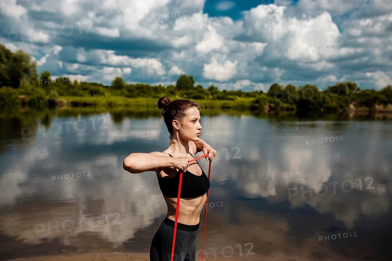 Athletic woman goes in for sports in nature in summer on the beach with resistance band