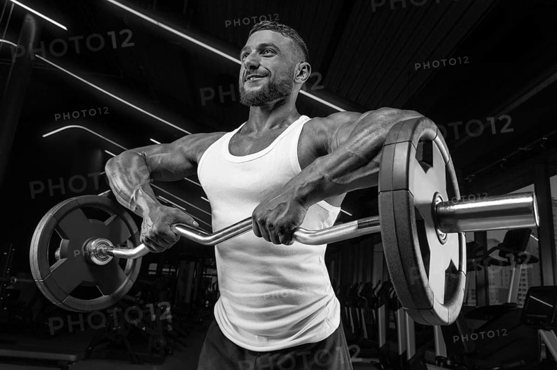 Handsome young man working out with a barbell in the gym. Shoulder pumping. Barbell pull to the chin. Fitness and bodybuilding concept
