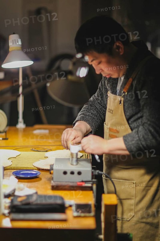 Asian Master luthier lute maker artisan both hands performing bend controller purfling strips process in iron tool for a new raw back and front plates of classic handmade violin in his workshop in Cremona