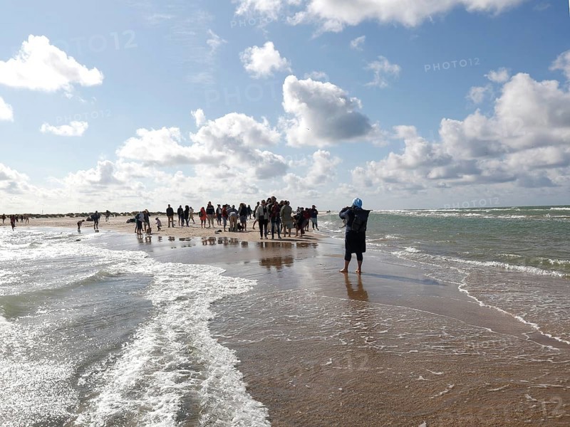 Tourists stand with one foot in the North Sea and one in the Baltic Sea in Grenen or Skagens Gren