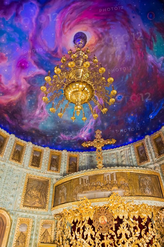 An opulent chandelier in a church with an illusionistic galaxy painted on the ceiling