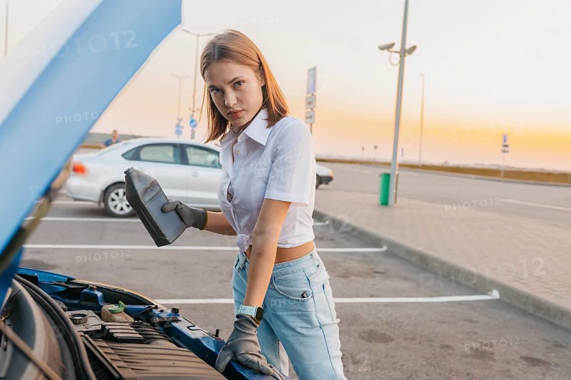 Young beautiful hot girl auto mechanic pours oil