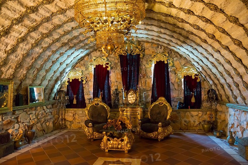 An opulently decorated room with throne chairs under a vaulted stone ceiling and a large chandelier