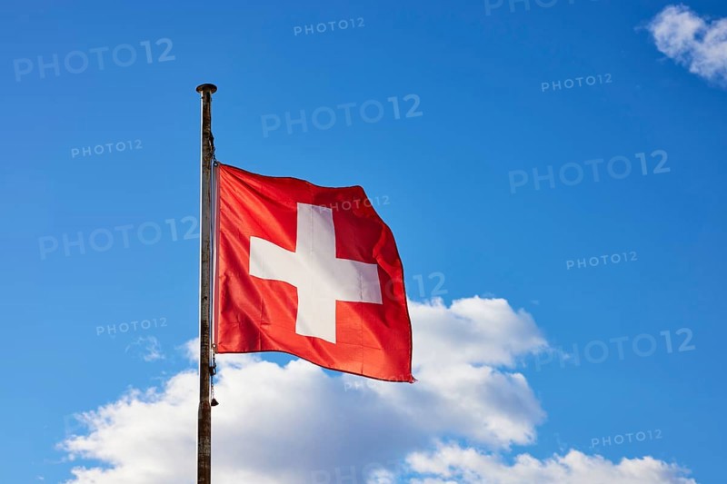 Swiss flag on a flagpole in front of a blue sky with white clouds in Ascona