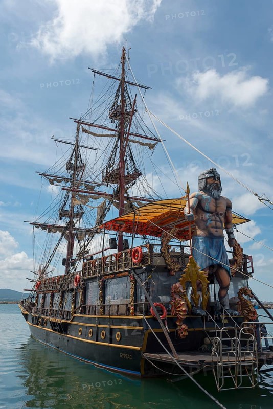 A large sailing ship with many masts and a pirate statue on board is anchored in the sea