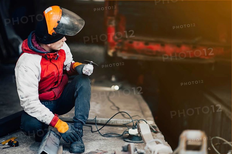 Man worker in a uniform and a mask works with a grinder