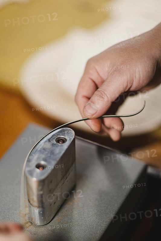 Unrecognizable luthier lute maker artisan both hands performing bend controller purfling strips process in iron tool for a new raw back and front plates of classic handmade violin in his workshop in Cremona