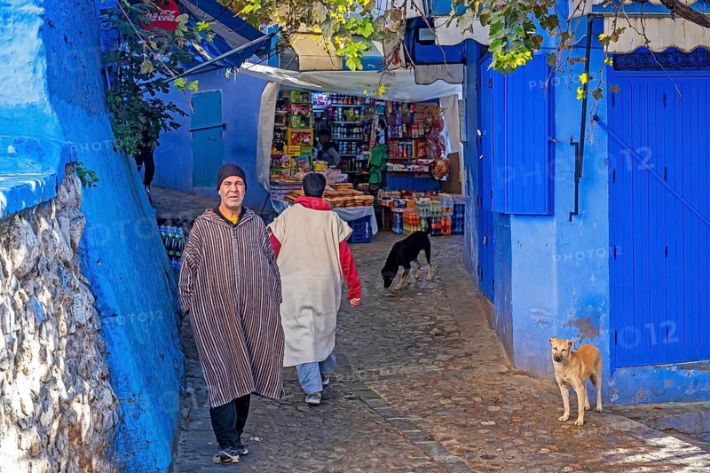 Muslim man wearing traditional djellaba and grocery shop in alleyway in blue medina