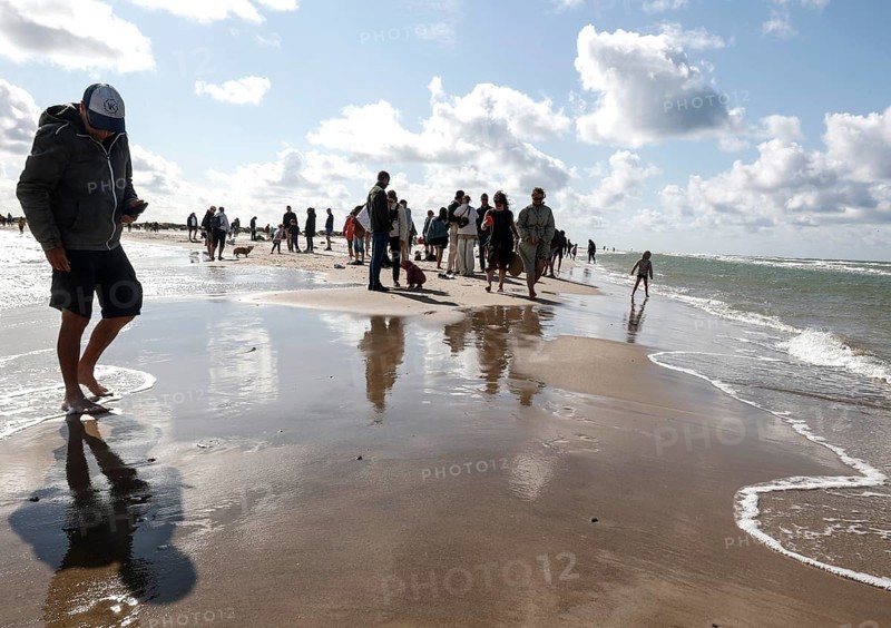 Tourists stand with one foot in the North Sea and one in the Baltic Sea in Grenen or Skagens Gren