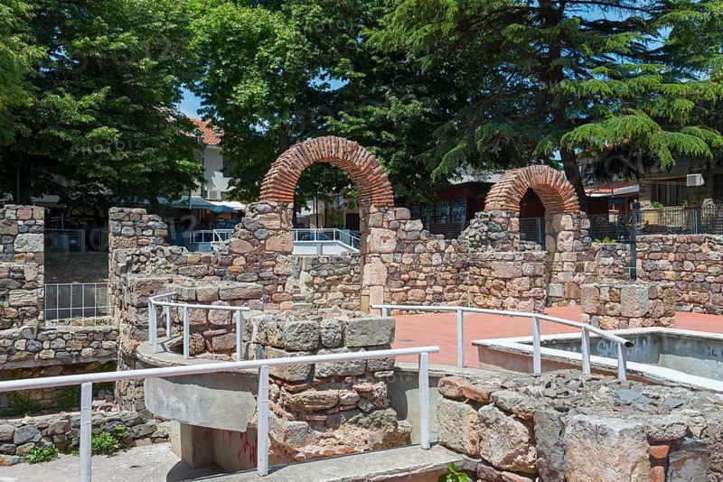 Ruins of an ancient structure with brick arches in an urban setting under a blue sky