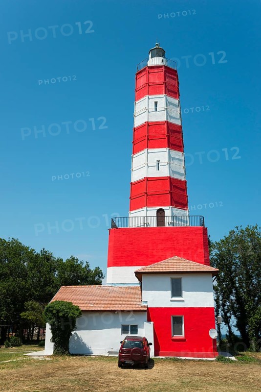 Red and white lighthouse against a clear blue sky with a red car in front of it