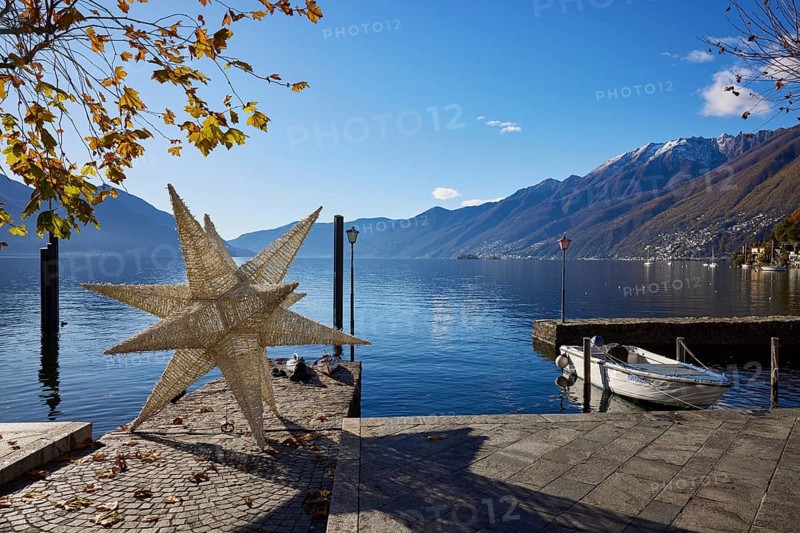Backlit photograph of the large Herrenhuth star as a Christmas decoration at the harbour entrance to Lake Maggiore with lanterns and motorboat in Ascona