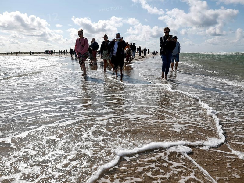 Tourists stand with one foot in the North Sea and one in the Baltic Sea in Grenen or Skagens Gren