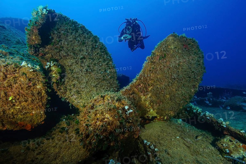 Diver swims behind huge propeller of sunken ship shipwreck wreck