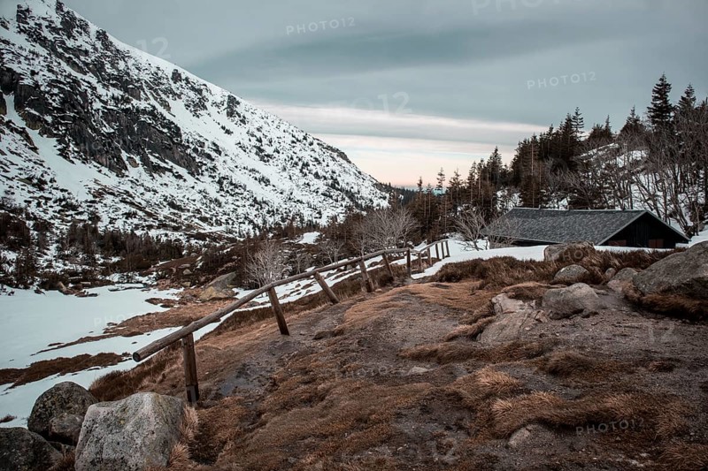 A serene winter landscape with a cabin, snow-covered mountain, and wooden fence at dusk. Poland, Karkonosze