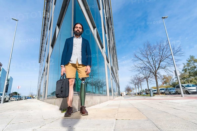 Businessman with prosthetic leg holding a laptop bag outside a financial building in the city