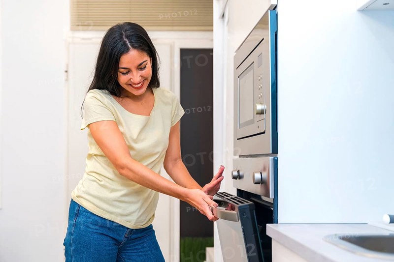 Casual smiling hispanic woman cooking pizza at home in the oven