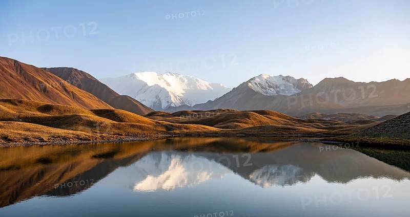 White glaciated and snowy mountain peak Pik Lenin at sunset, mountains reflected in a lake between golden hills, Trans Alay Mountains, Pamir Mountains, Osh Province, Kyrgyzstan, Asia