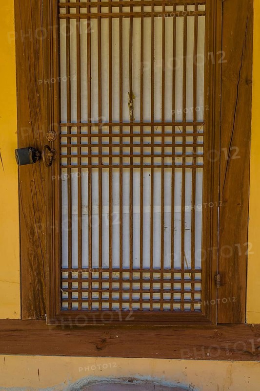 Oriental wooden slatted door of old stucco building with rice paper used for privacy on inside