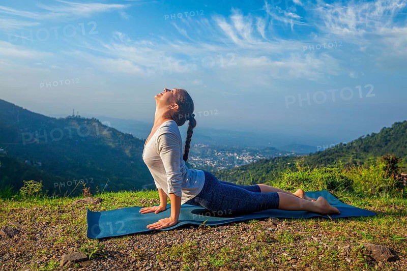 Yoga outdoors, woman practices Ashtanga Vinyasa yoga Surya Namaskar Sun Salutation asana Urdhva Mukha Svanasana, upward facing dog pose in mountains in the morning