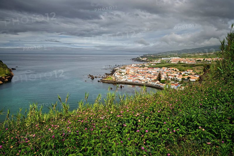 View of the town of Horta surrounded by green hills and cliffs under a cloudy sky, Monte da Guia, Horta, Faial, Azores, Portugal, Europe