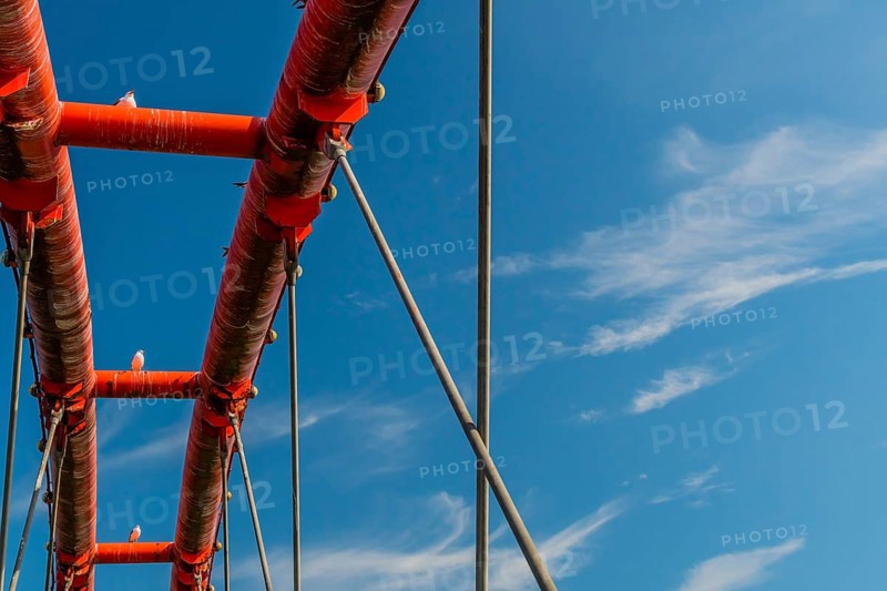 Three seagulls perched on top of dirty orange bridge with beautiful blue sky in background