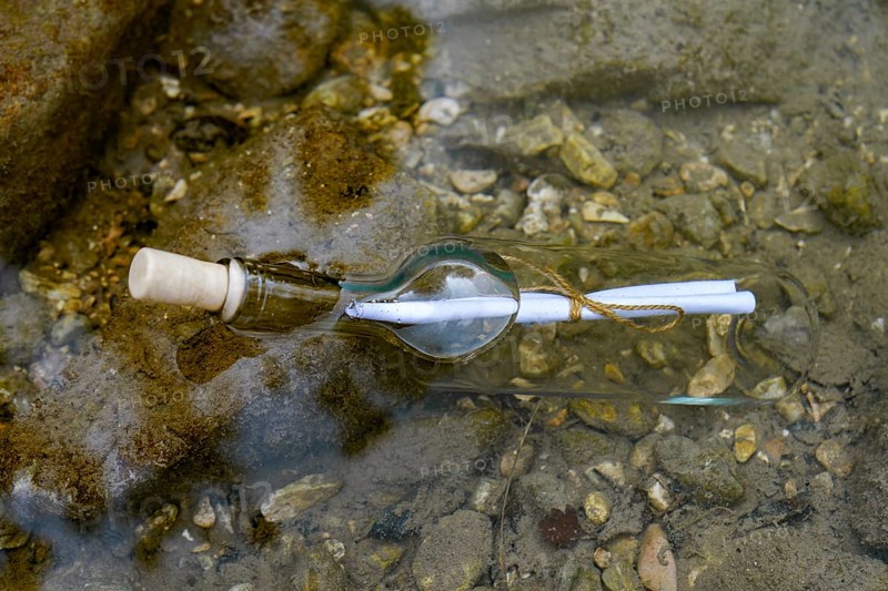Message in a bottle floating in the water on the rocks at the seashore