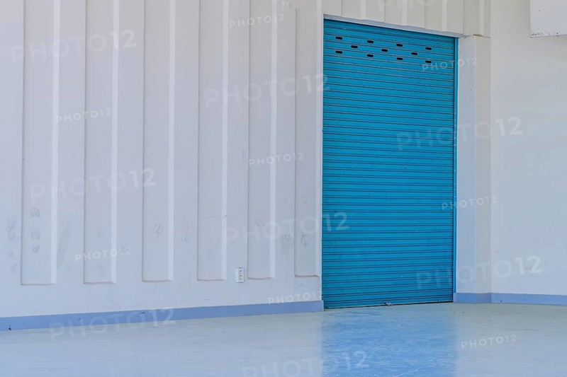 Large blue metal door in white wall reflecting onto concrete floor of amphitheater in urban public park