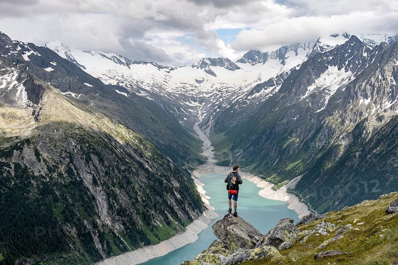 Mountaineer on a rock in front of a mountain panorama, view of Schlegeisspeicher, glaciated rocky mountain peaks Hoher Weisszint and Hochfeiler with glacier Schlegeiskees, Berliner Hoehenweg, Zillertal Alps, Tyrol, Austria, Europe