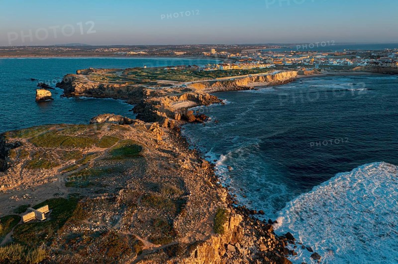 Sunset landscape of peninsula, bay and town of Peniche, Portugal. Summer sunset haze, little foliage and rocky cliffs, peninsula and rocks, fishing town, horizon, aerial shot, drone point of view