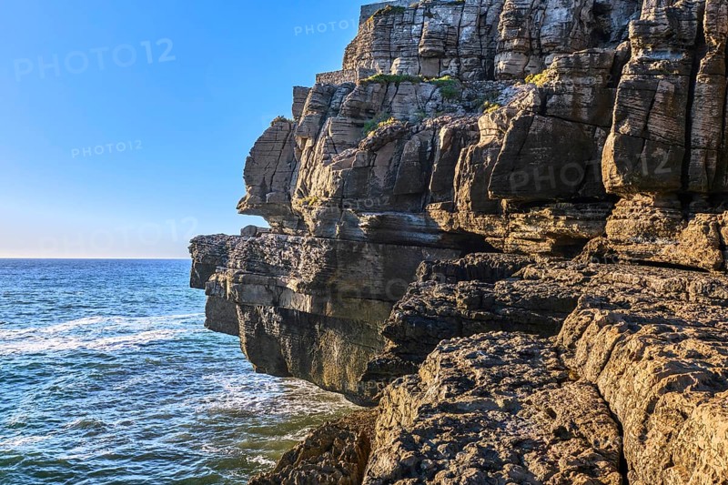 Beautiful cliffs and rock formations in Peniche, Portugal, on sunny day. Weathered rock formations, geological interest, cliffs, blue sea waves, tide, coastline, clear blue sky, Europe