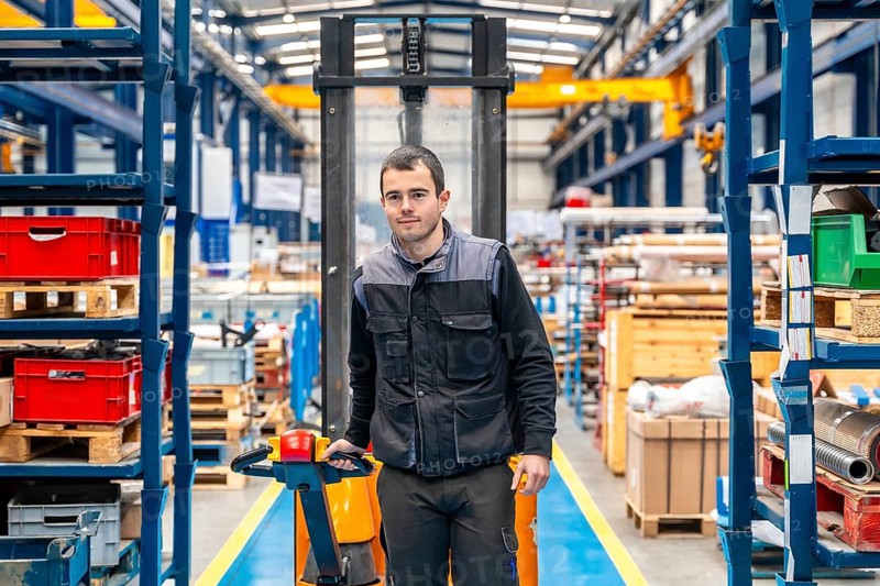 Frontal view of a male worker walking among shelves with handcart in a warehouse