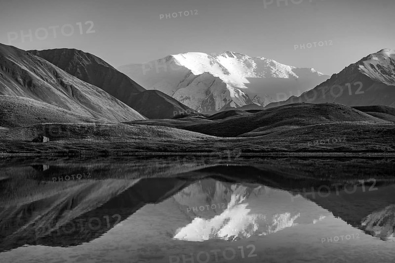 White glaciated and snowy mountain peak Lenin Peak at sunset, mountains reflected in a lake between golden hills, black and white photograph, Trans Alay Mountains, Pamir Mountains, Osh Province, Kyrgyzstan, Asia