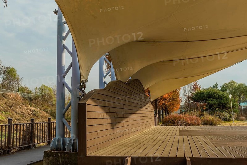 Closeup side view of wooden outdoor stage with white canvas awning in public park