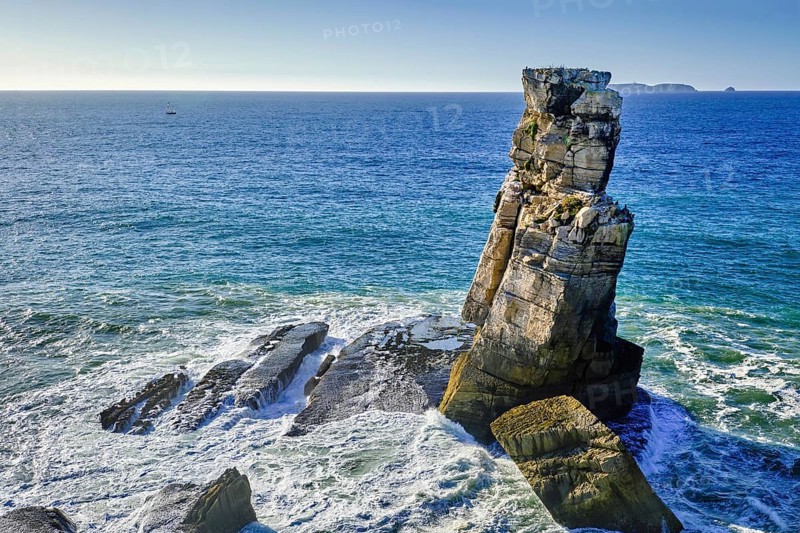 Blue sea waves beat against Nau dos Corvos or Crows nest rock near Peniche peninsula, Portugal at sunny day. Atmospheric haze, Berlengas islands, Cabo Carvoeiro viewpoint, travel destination, Atlantic ocean coast
