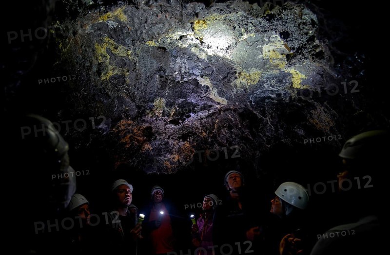A group of people in helmets listen to a guide in the lava tunnel Gruta das Torres, Gruta das Torres, Pico, Sao Miguel, Faial, Azores, Portugal, Europe