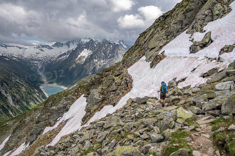 Two mountaineers on hiking trail with snow, view of Schlegeisspeicher, glaciated rocky mountain peaks Hoher Weisszint and Hochfeiler with glacier Schlegeiskees, Berliner Hoehenweg, Zillertal Alps, Tyrol, Austria, Europe