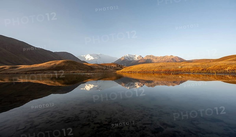 White glaciated and snowy mountain peak Pik Lenin at sunrise, mountains reflected in a lake between golden hills, Trans Alay Mountains, Pamir Mountains, Osh Province, Kyrgyzstan, Asia