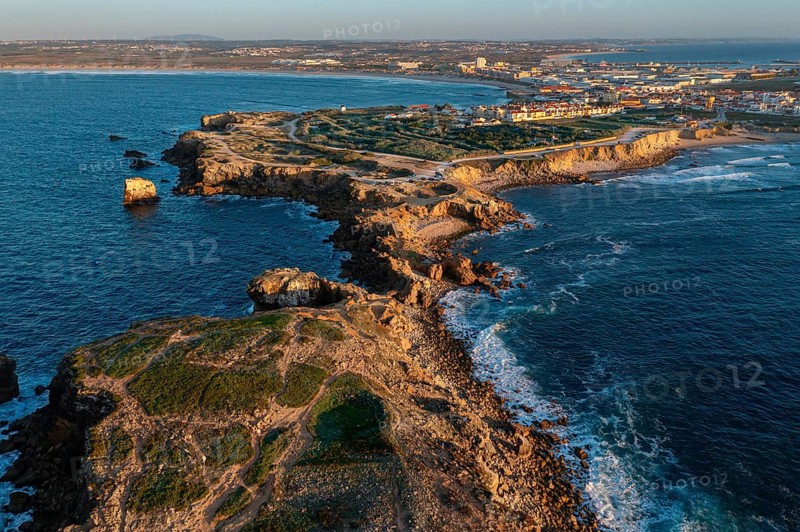 Aerial landscape of Peniche, Portugal, peninsula and town at sunset. Summer sunset haze, little foliage and rocky cliffs, peninsula and rocks, fishing town, horizon, Europe