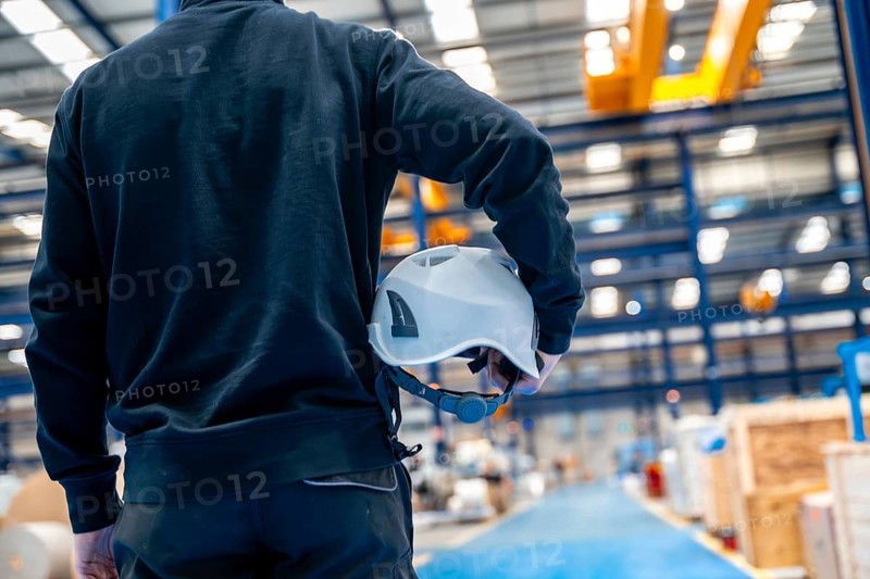Rear view of an unrecognizable worker holding a helmet in a factory