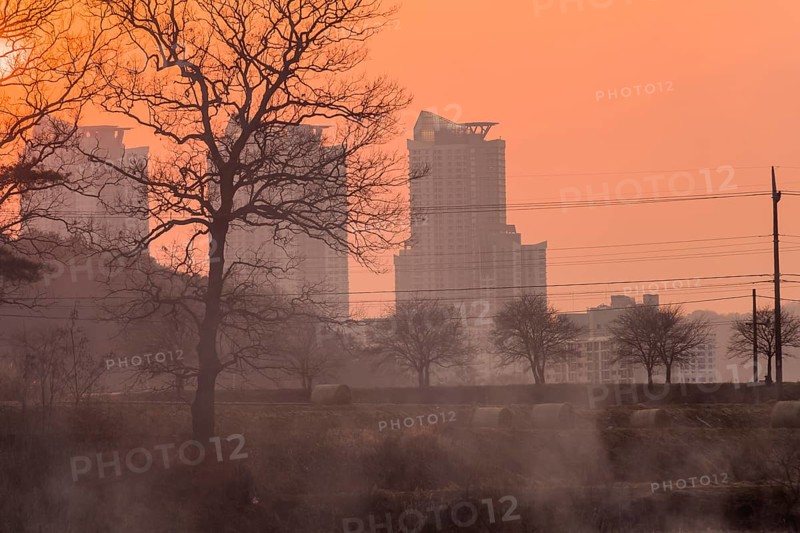 Smoke in the air at sunset obscures the view of apartments and trees and creates a halloween like orange glow in the sky