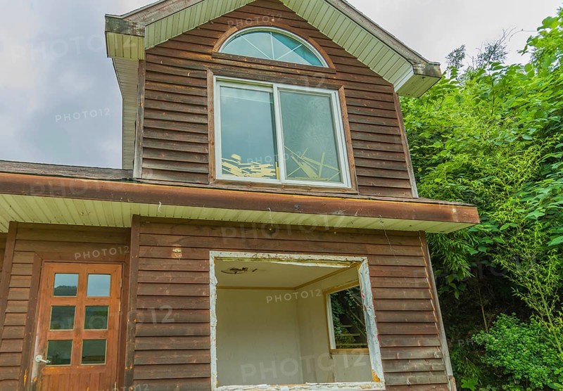 View of window on second story, front door and first floor window frame of abandoned house in countryside