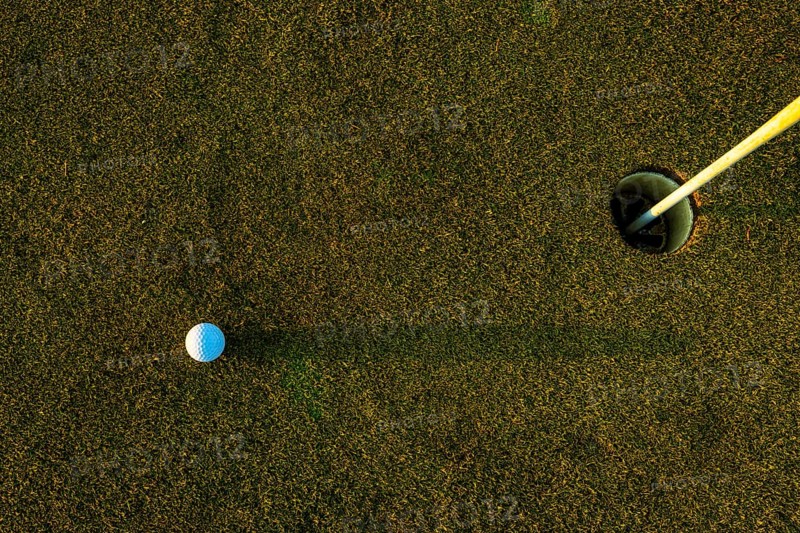 Golf Ball on the Grass with Shadow and Hole with Flag Pole on Putting Green on Golf Course in Sunset in Switzerland