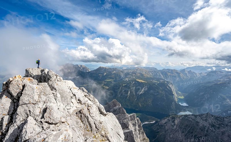 Mountaineer on the rocky summit of the Watzmann Mittelspitze, Watzmann crossing, view of mountain panorama with Steinernes Meer and Koenigssee, Berchtesgaden National Park, Berchtesgaden Alps, Bavaria, Germany, Europe