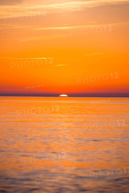 Intense, atmospheric sunset with bright orange-yellow sky over the Baltic Sea, only a small part of the sun disc still visible above the sea horizon, calm water, Hiddensee Island, Mecklenburg-Western Pomerania, Germany, Europe