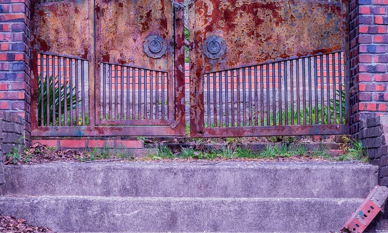 View of stairs leading to a chained rusted gate with red brick columns on each side located at old abandoned picnic pavilion in woodland area in South Korea